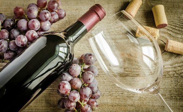 Bottiglia di vino rosso con calice e grappoli d'uva per scegliere il vino ideale da utilizzare in cucina